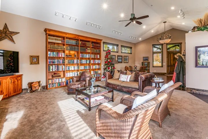 Spacious living area featuring a full-height built-in wood bookcase, vaulted ceilings, recessed lighting, a ceiling fan, and wood-trim windows
