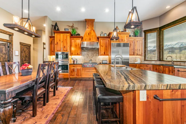 Gourmet kitchen and dining area featuring rich wood-finish flooring, custom wood cabinetry, and a substantial island with stone countertop