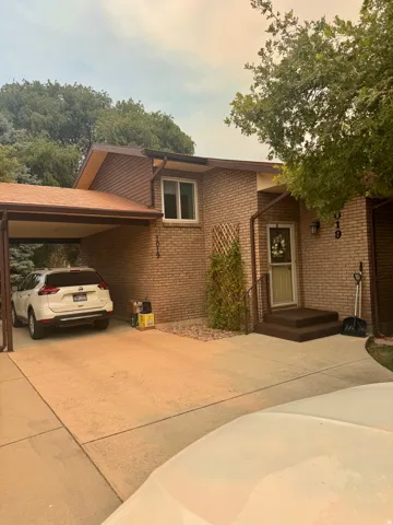 Brick exterior featuring a covered carport, concrete driveway, and mature landscaping