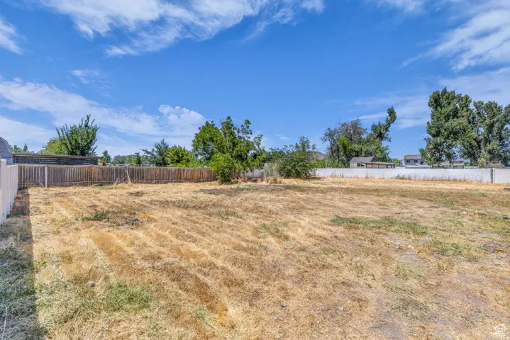 Expansive lot featuring a varied perimeter fence line, clear blue sky, and mature trees in the background