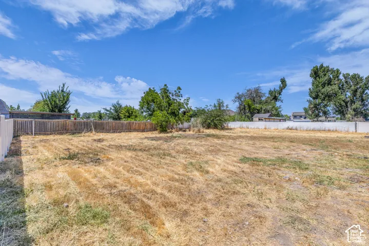 Expansive lot featuring a varied perimeter fence line, clear blue sky, and mature trees in the background