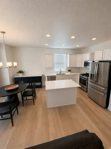 Kitchen featuring a central island with white countertop, stainless steel appliances, recessed lighting, wood-finish flooring, and white cabinetry