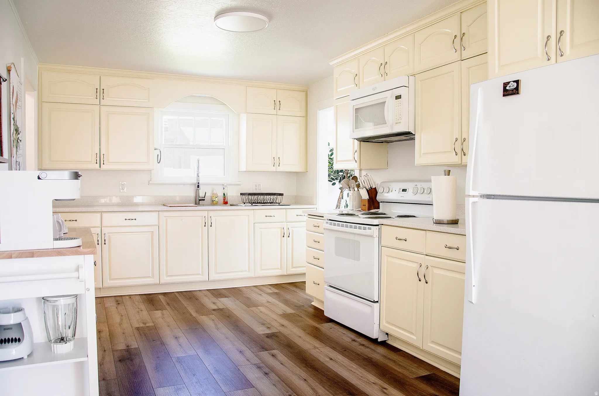Kitchen featuring extensive cream cabinetry, wood-finish flooring, and white countertops