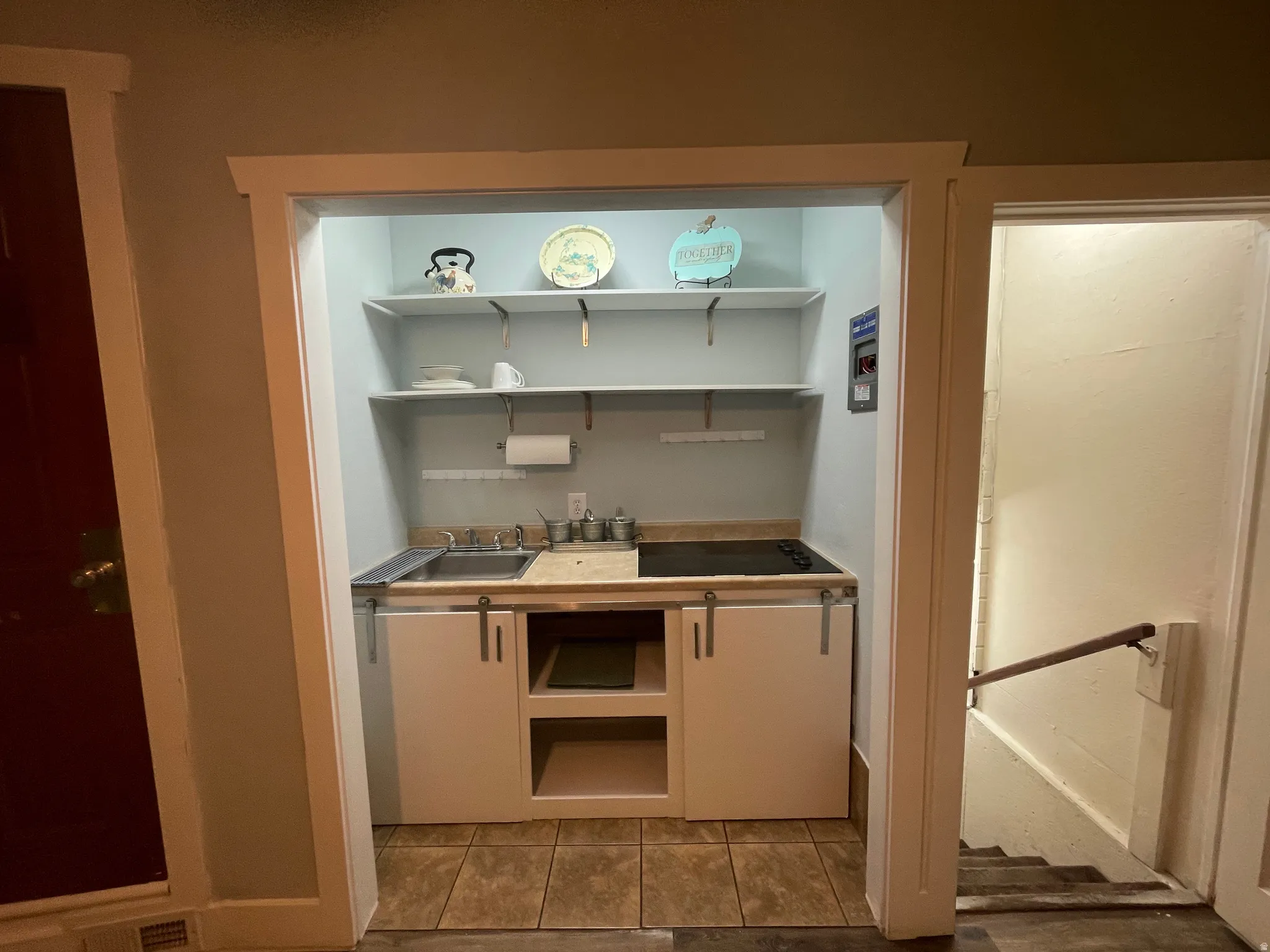Compact kitchen area featuring a built-in sink, integrated cooktop, and open shelving
