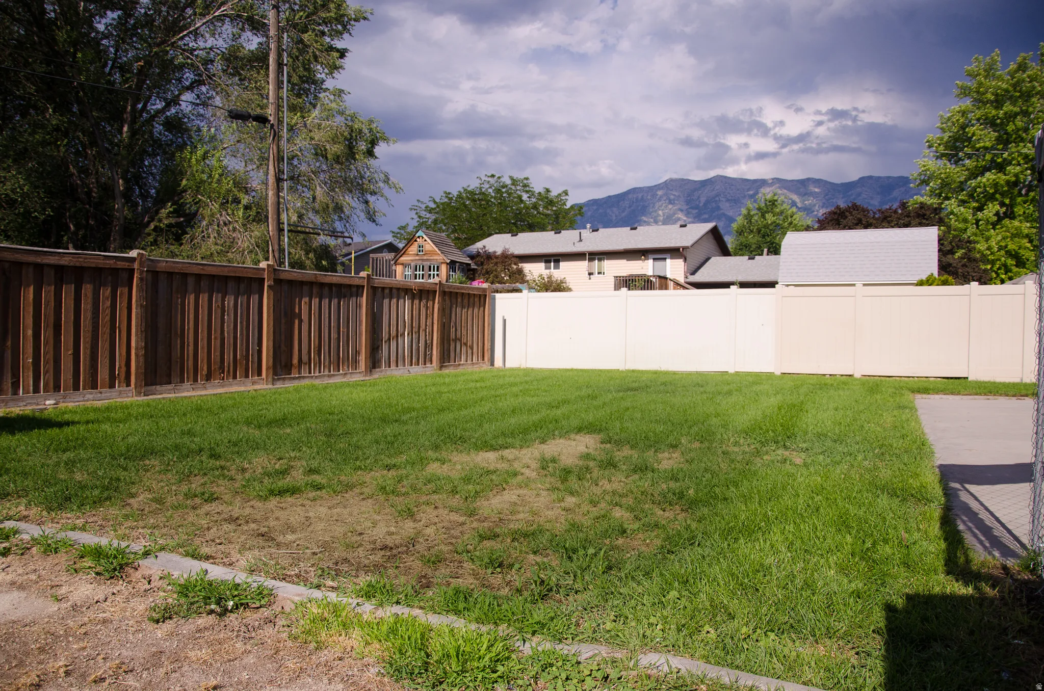 Expansive backyard featuring a manicured lawn, a wood privacy fence, and a light-colored solid fence