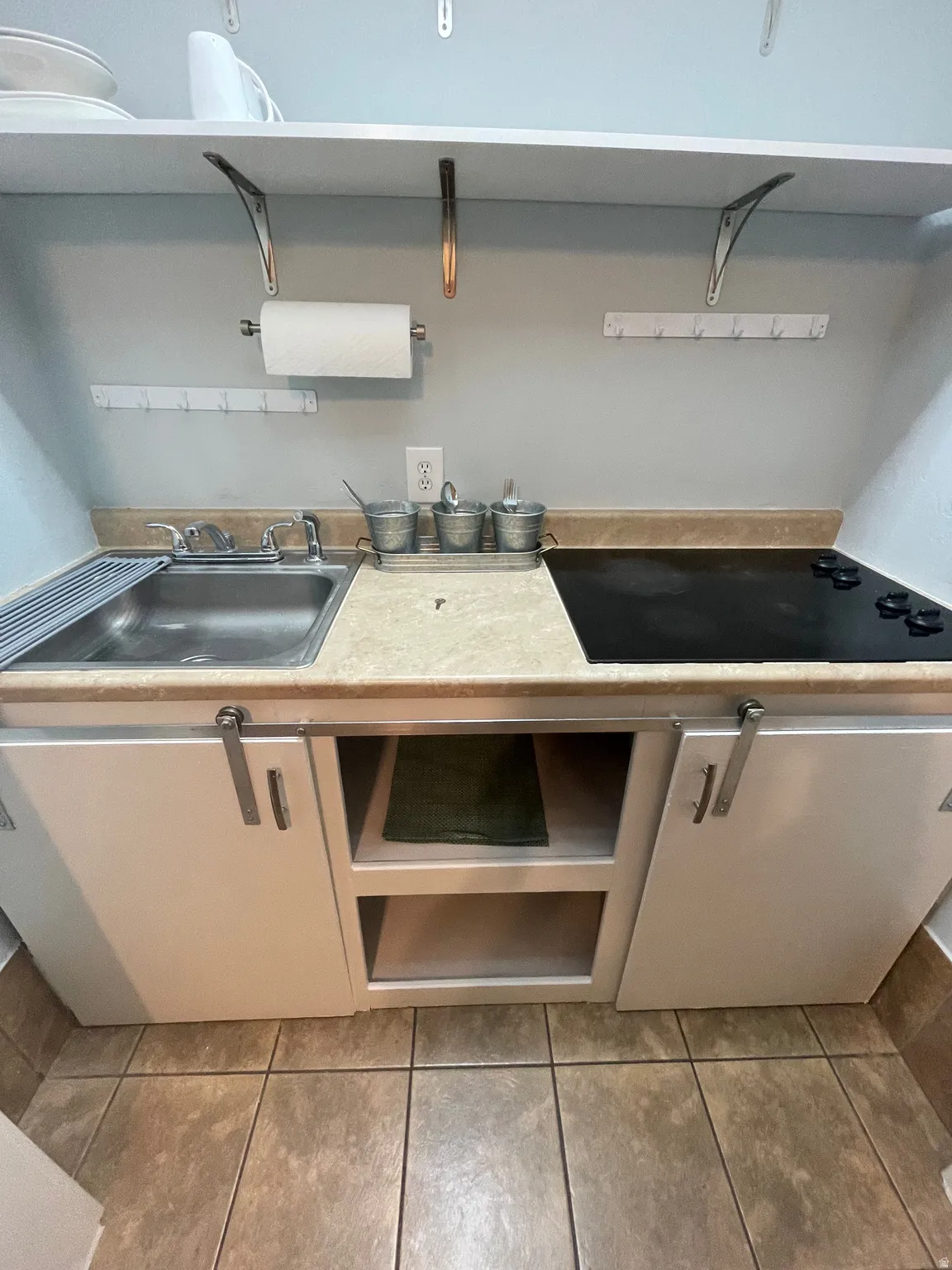 Compact kitchen area featuring a stainless steel sink, solid surface countertop, and a built-in electric cooktop