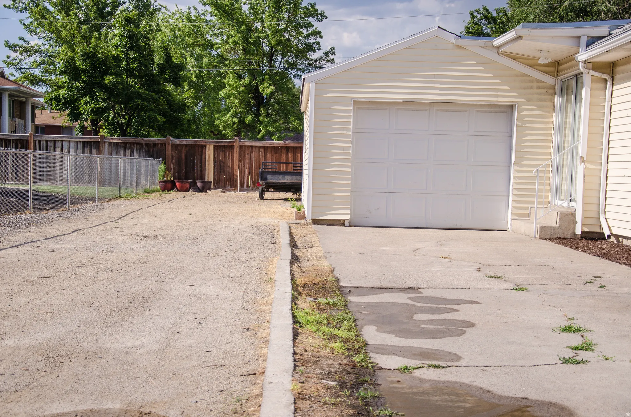 Detached garage with horizontal siding, concrete driveway, and gravel parking area