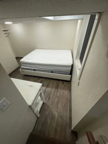 Compact room featuring wood-finish flooring, white painted walls, and a window with a white frame