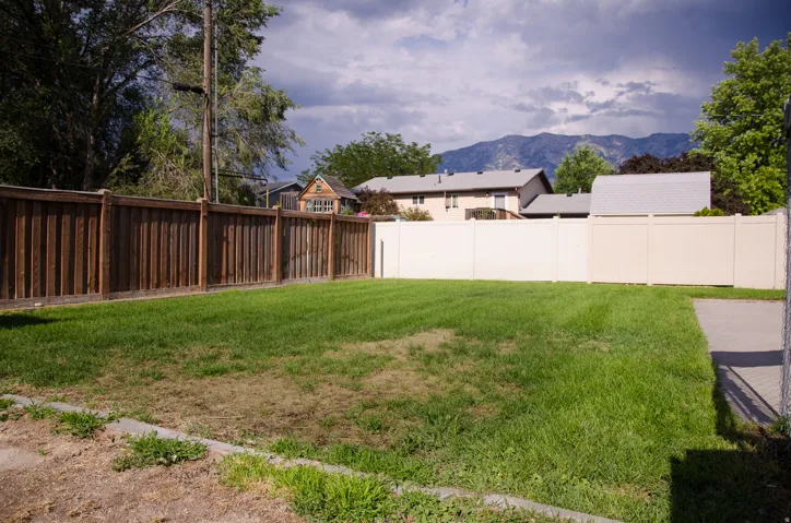 Expansive backyard featuring a manicured lawn, a wood privacy fence, and a light-colored solid fence
