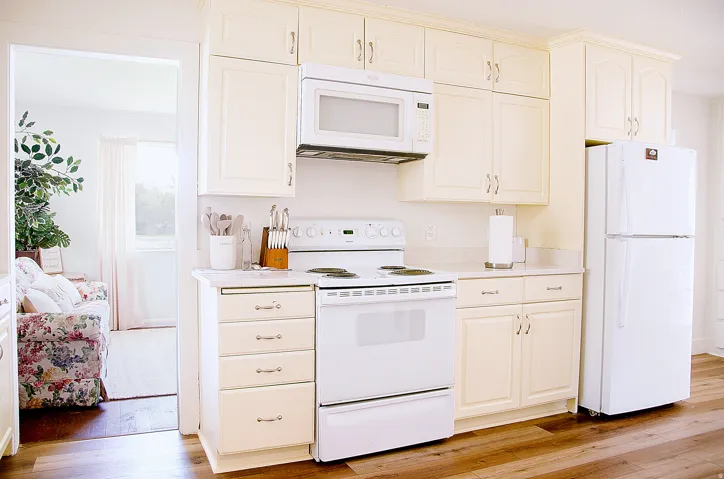 Kitchen featuring cream-toned cabinetry with brushed nickel hardware, white appliances, and wood-finish flooring