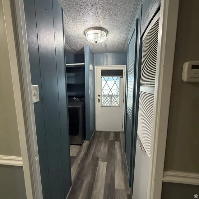 Hallway featuring wood-finish flooring, a flush-mount ceiling light fixture, a white door with decorative glass inserts, and a built-in shelving unit, a storm door, extra area for storage or cabinet along with washer and dryer.