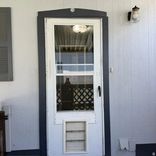 White storm door with a full-length glass panel and integrated pet door, framed by dark trim. This is in the carport area leading into the mudroom/Laundry room