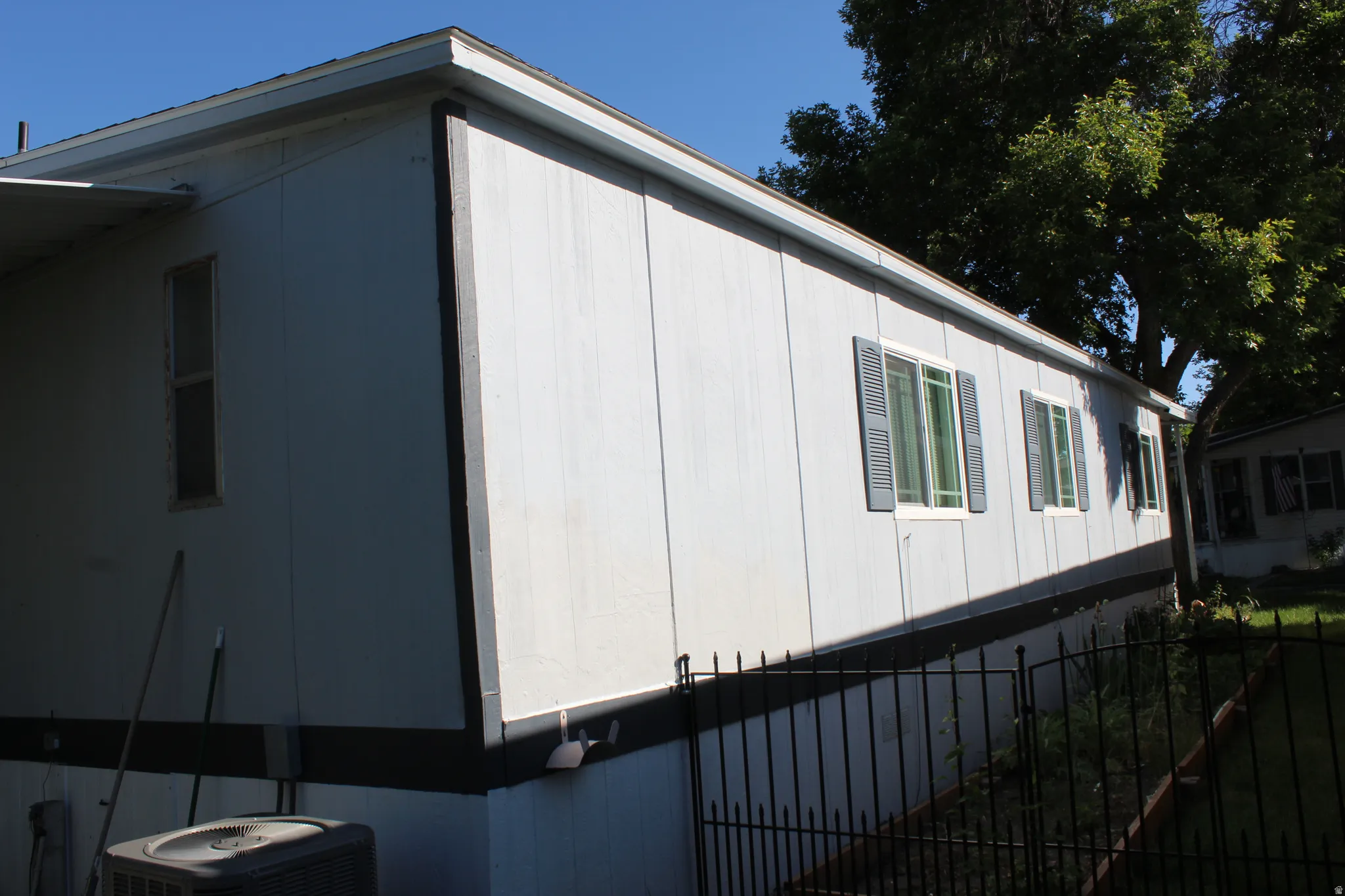 Single-story exterior with light-colored vertical siding, contrasting dark trim, and multiple windows featuring louvered shutters