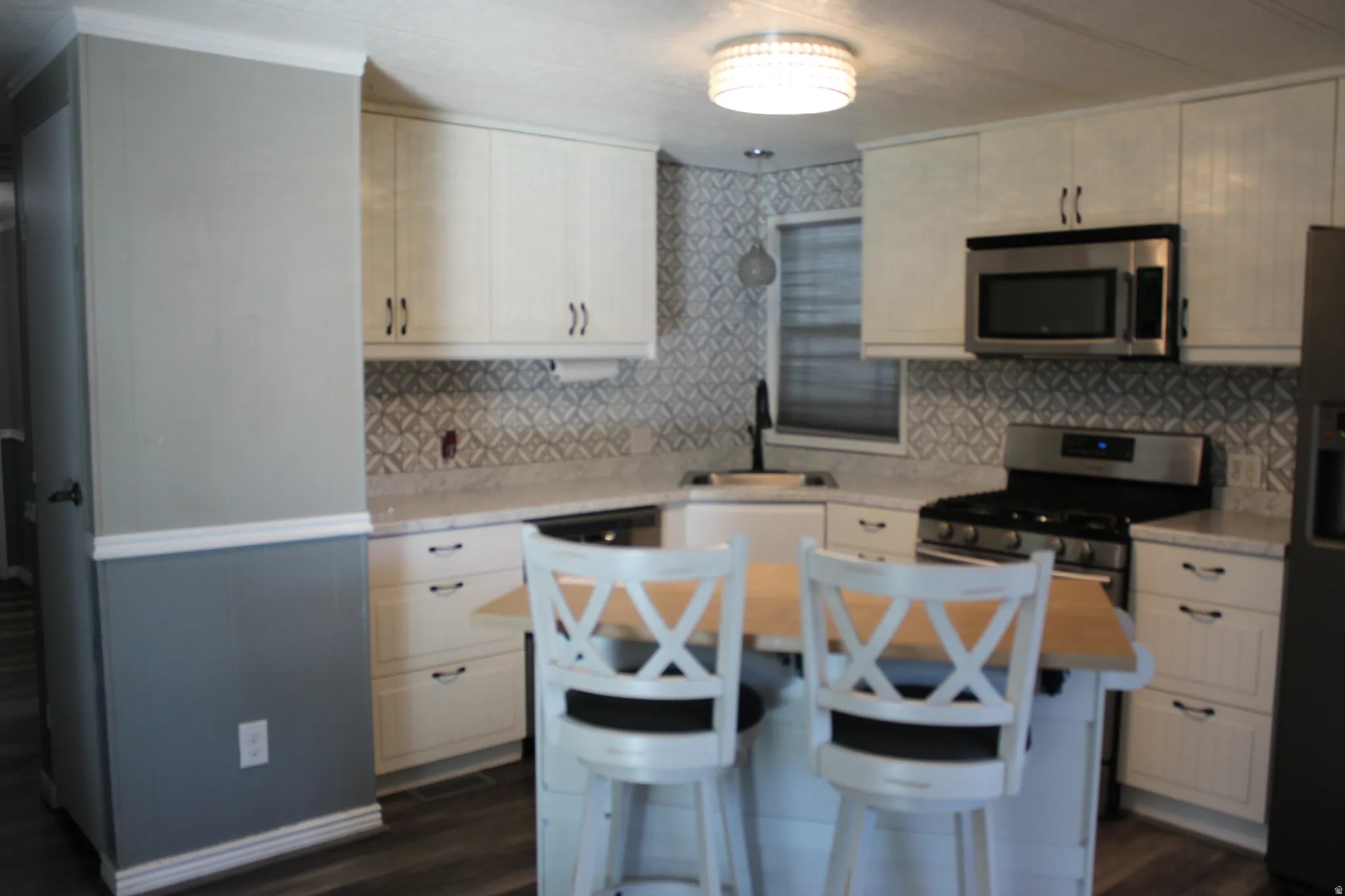 Kitchen featuring white cabinetry, light countertops, a patterned tile backsplash, stainless steel appliances, and wood-finish flooring