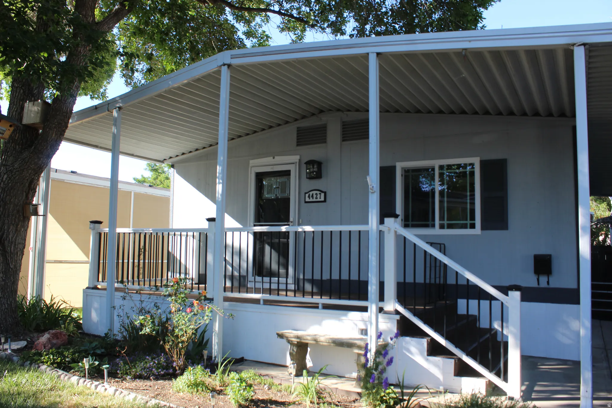Covered front porch with a metal roof, storm door, & white support columns. with a large tree with bird houses.