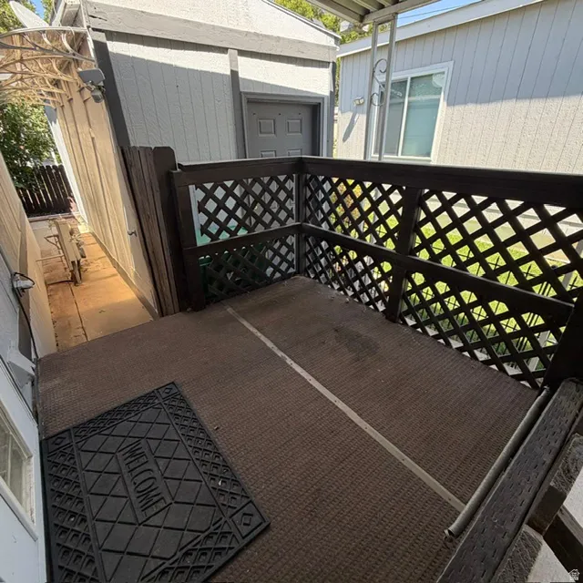 Outdoor patio space featuring a brown lattice railing and a brown textured floor. At the end of the driveway.