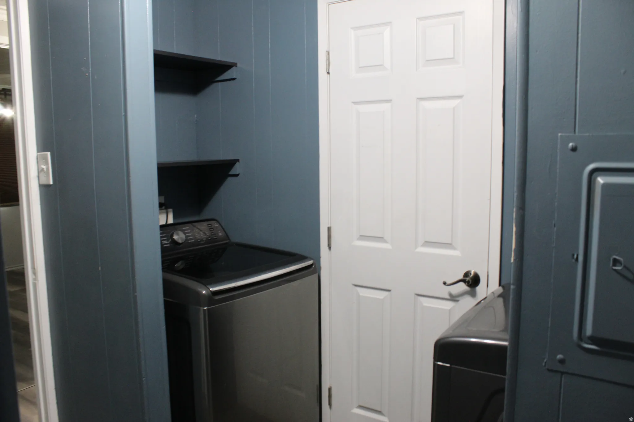 Dedicated laundry area featuring a top-loading appliance, wall-mounted shelving, and paneled walls