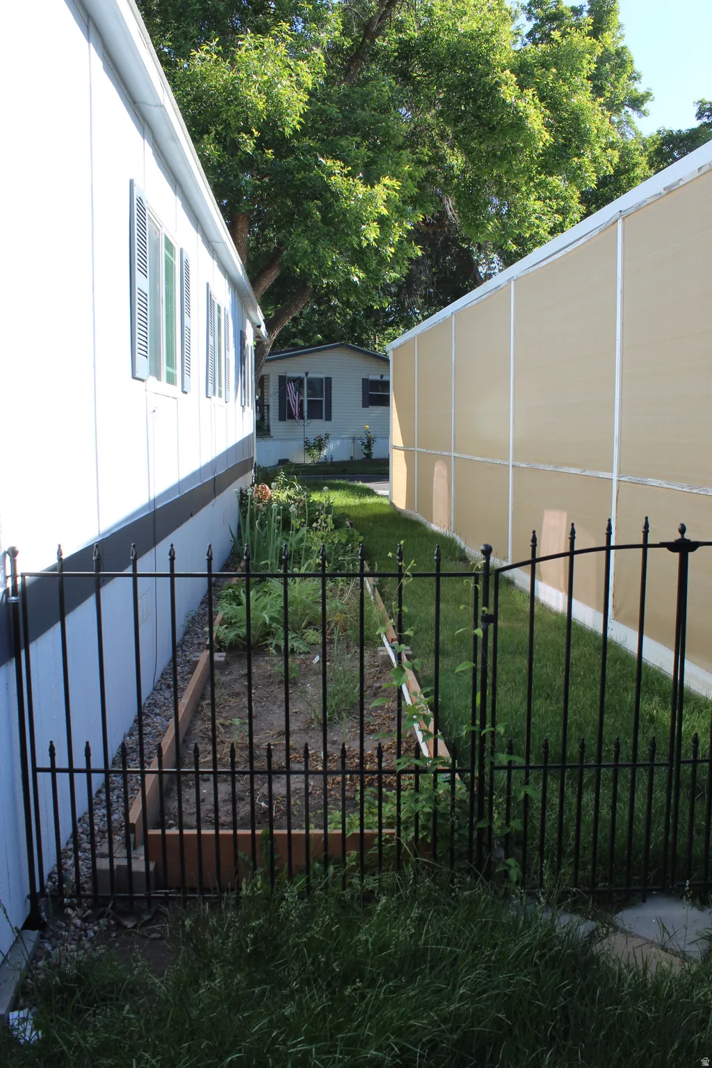 Private side yard featuring a black wrought-iron fence with a hinged gate, an enclosed garden bed, and mature trees providing natural shade