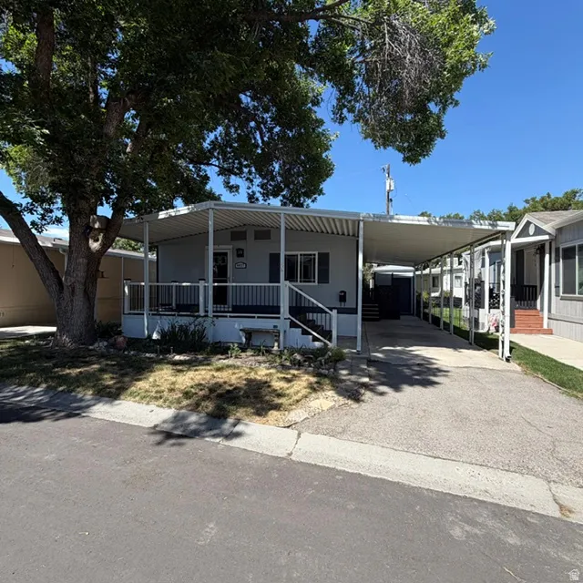 Light gray exterior with a covered front porch, white railing, dark shutters  & covered parking space.