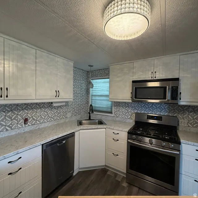 Upclose view of the kitchen.Updated kitchen featuring white cabinetry, stainless steel appliances, patterned tile backsplash, light-toned countertops, and wood-finish flooring