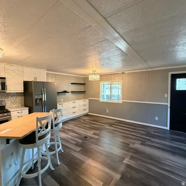 Open-concept living space with wood-finish flooring, white cabinetry, integrated kitchen appliances, and a decorative light fixture