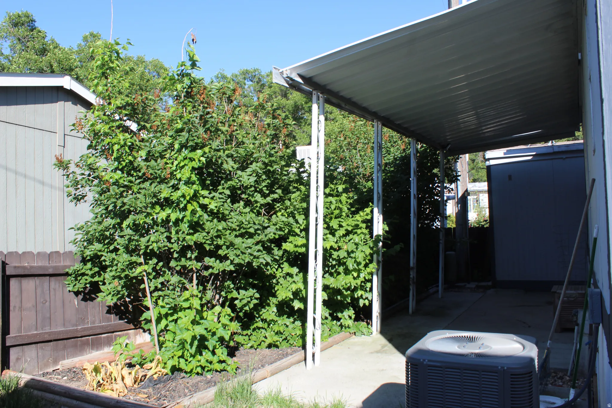 Exterior patio area featuring a metal awning structure, concrete slab, and an adjacent wood fence