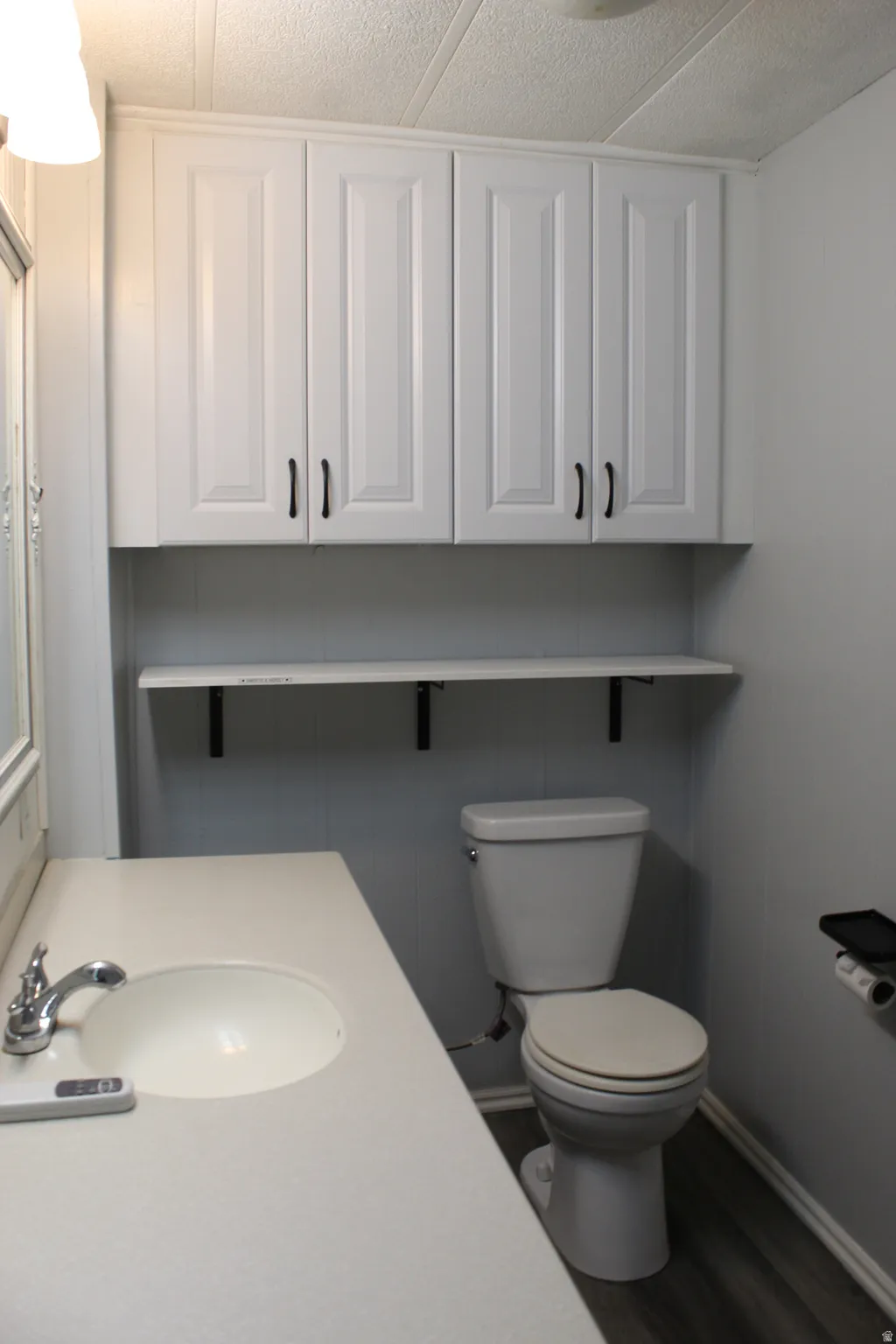Primary Bathroom featuring white cabinetry with dark hardware, a white built-in sink, a neutral countertop, and wood-finish flooring