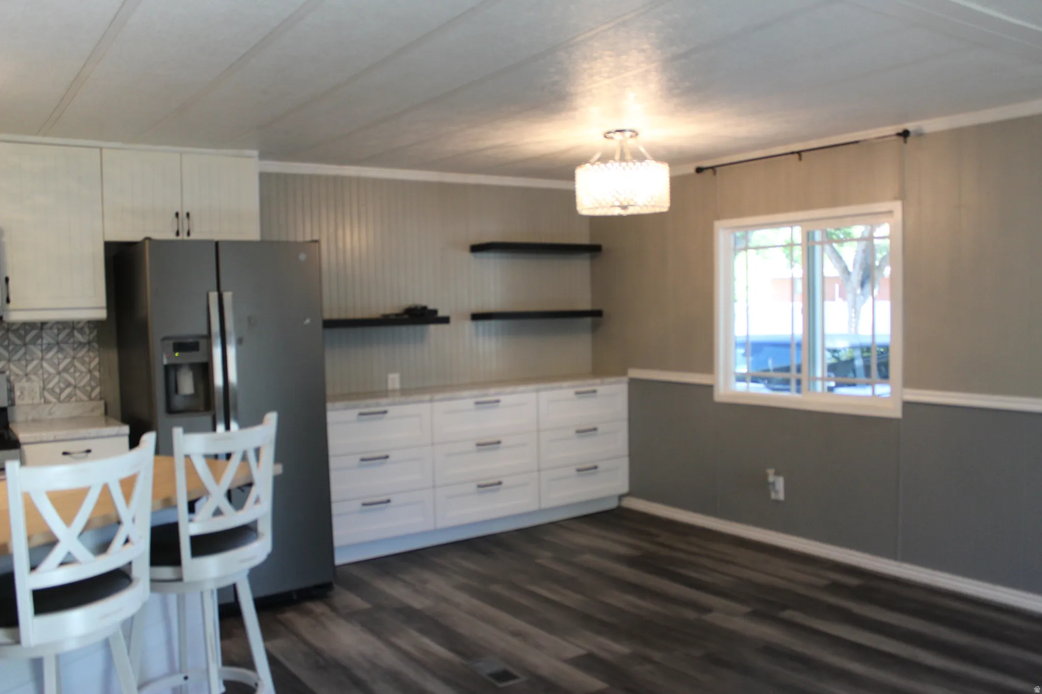 Open-concept living space featuring wood-finish flooring, a contemporary chandelier, and a bright window
