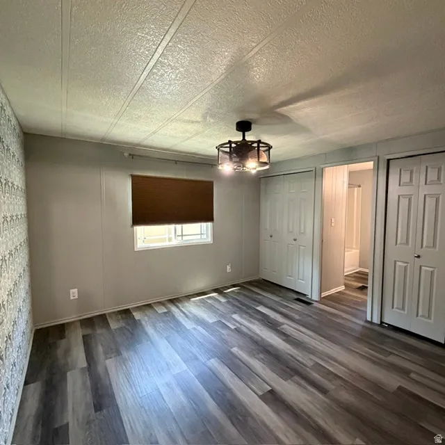 Primary bedroom with view in ensuite Spacious room featuring multi-tone wood-finish flooring, a contemporary ceiling light fixture, a window with a brown roll-down shade, and multiple closet storage options with bi-fold doors