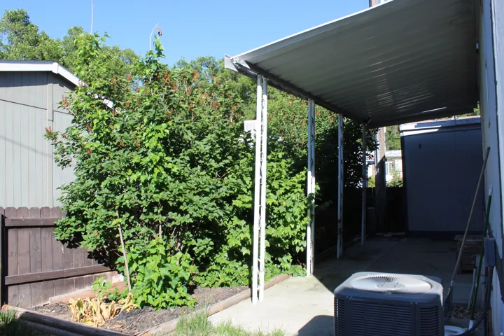 Exterior patio area featuring a metal awning structure, concrete slab, and an adjacent wood fence