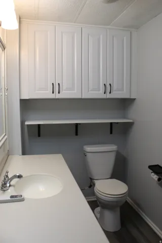 Primary Bathroom featuring white cabinetry with dark hardware, a white built-in sink, a neutral countertop, and wood-finish flooring