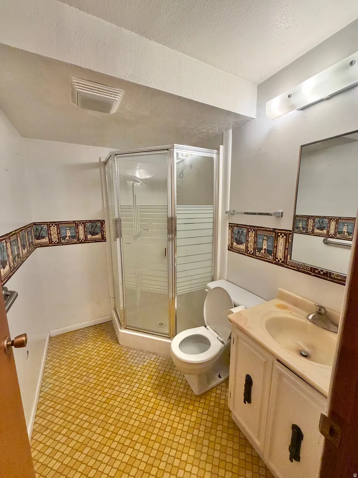 Compact bathroom featuring a corner shower enclosure, white vanity with integrated sink, and patterned floor tile