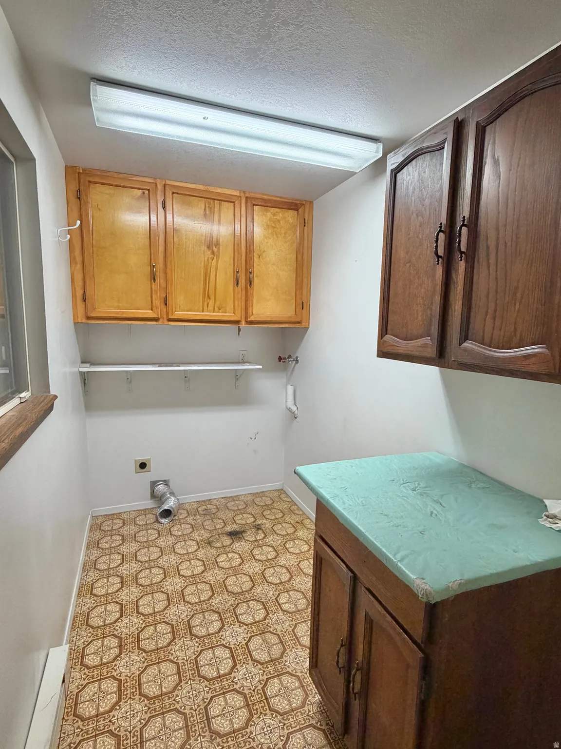 Dedicated utility area featuring patterned flooring, wood cabinetry, and a countertop