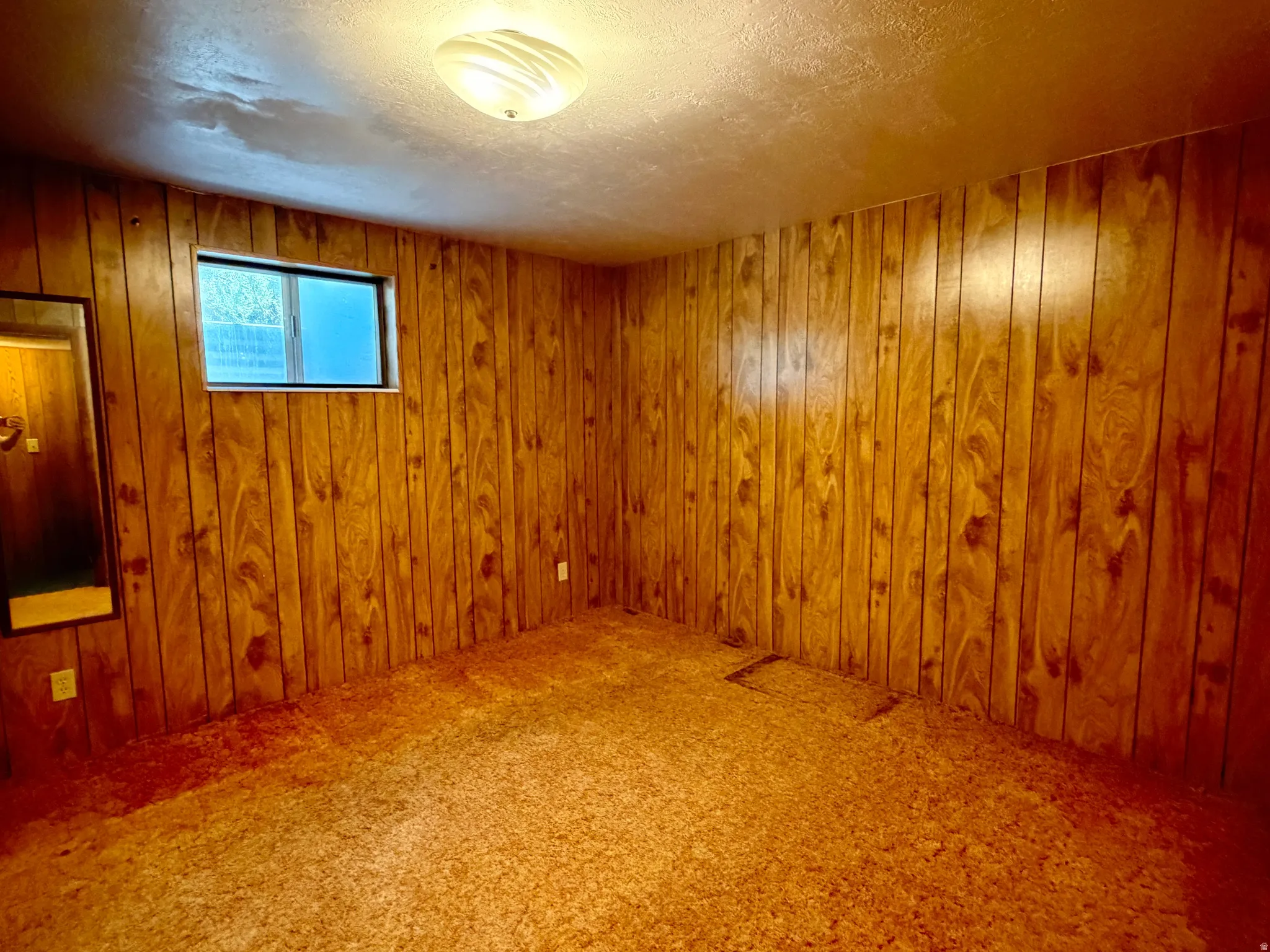 Wood paneling walls with window, textured ceiling, and flush mount lighting
