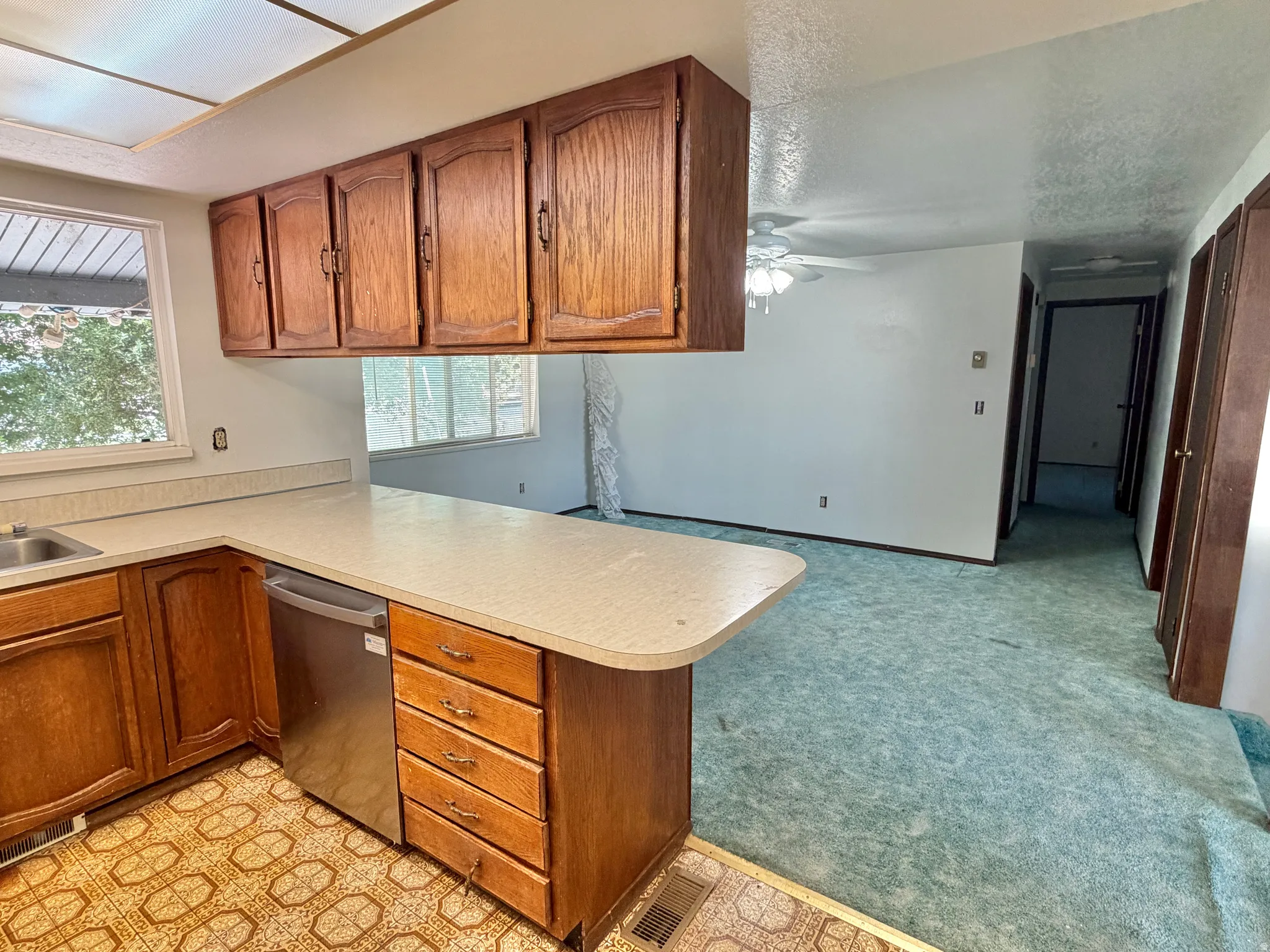 Kitchen with wood cabinetry, light-toned countertops, and a stainless steel dishwasher