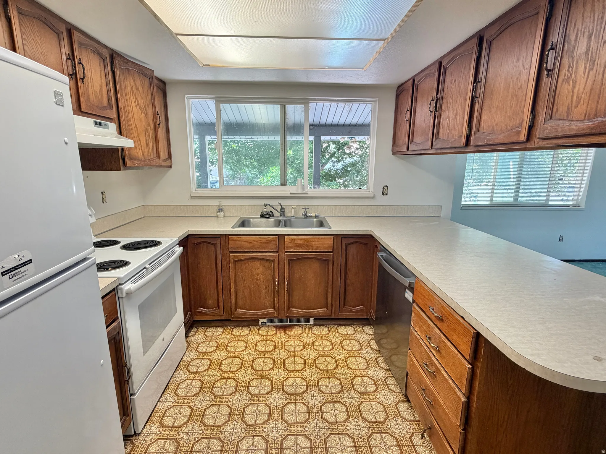 Kitchen featuring wood-finish cabinetry, light countertops, and a double-basin stainless steel sink