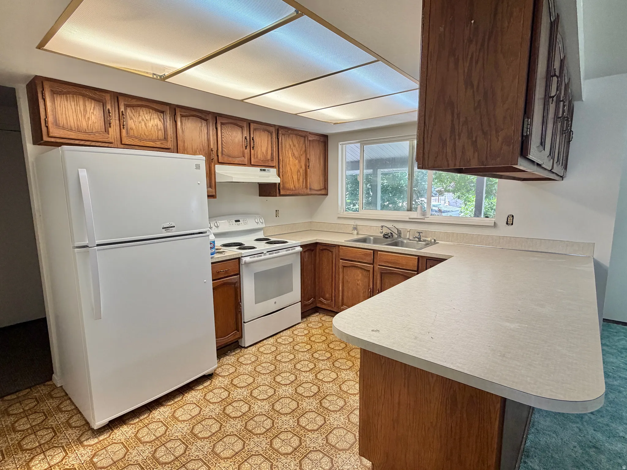 U-shaped kitchen featuring wood cabinetry, light-toned countertops, and an integrated double-basin sink
