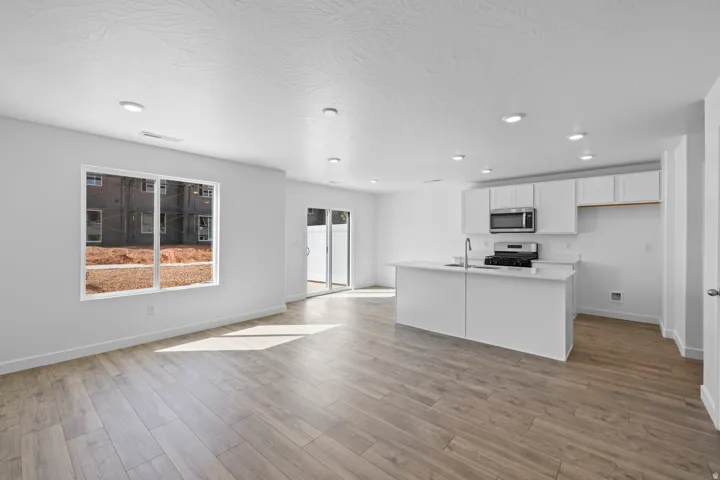 Open-concept living space featuring wood-finish flooring, recessed lighting, and a kitchen island with a stainless steel sink