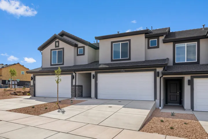 Modern stucco exterior with dark trim accents, featuring attached garages, a dark entry door, and stone veneer detailing