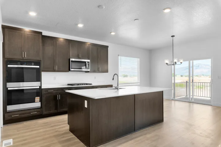 Modern kitchen featuring dark wood-finish cabinetry, white countertops, built-in double ovens, a central island with an integrated sink, and wood-finish flooring