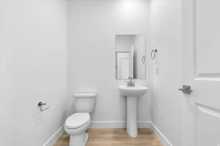 Bathroom featuring a pedestal sink with a chrome faucet, rectangular wall-mounted mirror, and wood-finish flooring