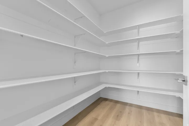 Spacious walk-in pantry featuring extensive white shelving, wood-finish flooring, and ample storage capacity