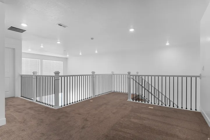 Spacious loft area featuring plush brown carpeting, contemporary white walls, and recessed lighting