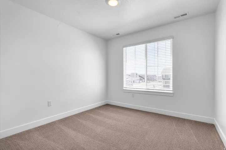 Carpeted room featuring a large window with blinds, white walls, white baseboards, and a ceiling light fixture