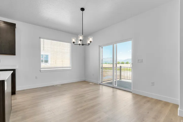 Dining area featuring light wood-finish flooring, a modern black chandelier with glass shades, a window with horizontal blinds, and sliding glass doors opening to an exterior balcony with metal railings