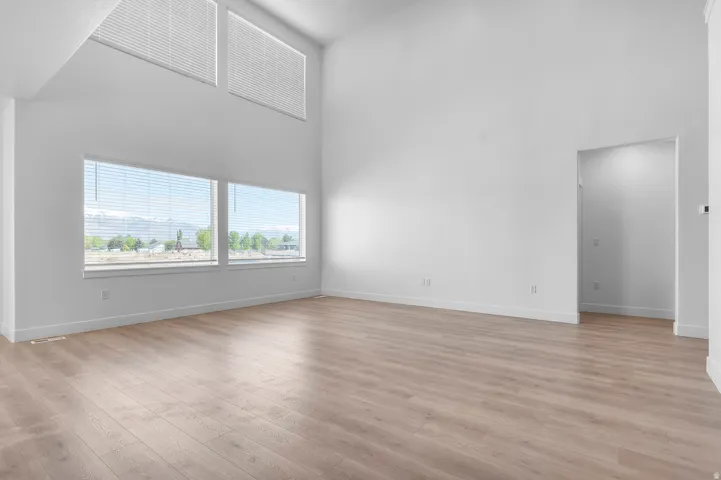 Open-concept room featuring high vaulted ceilings, multiple large windows with slat blinds, light wood-finish flooring, and white baseboards