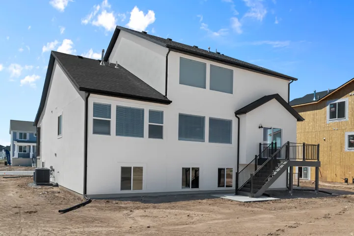 Rear exterior featuring a white stucco finish, dark shingle roof, and multiple large windows