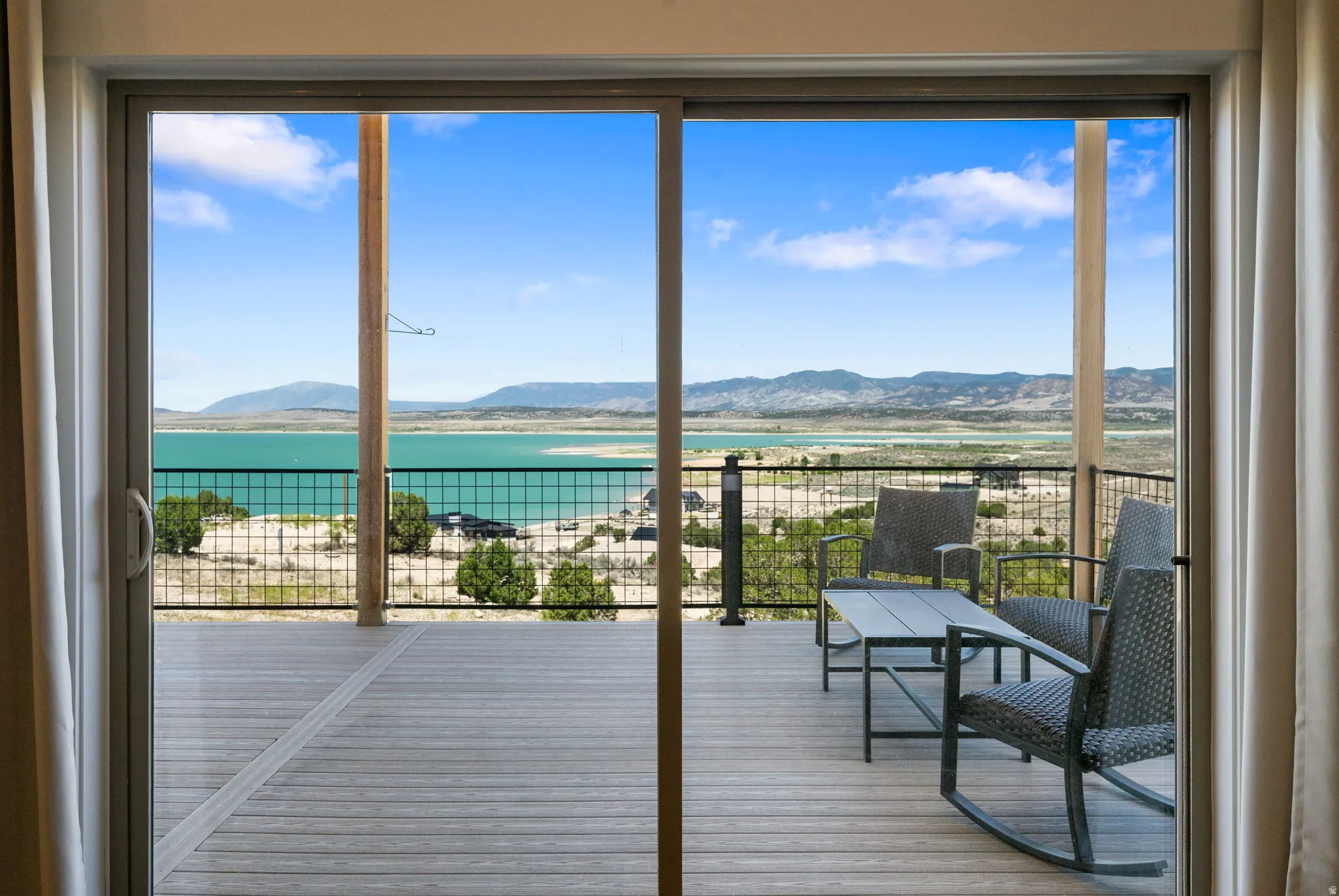 Sliding glass doors opening to an outdoor deck with metal railing overlooking a body of water and distant mountains