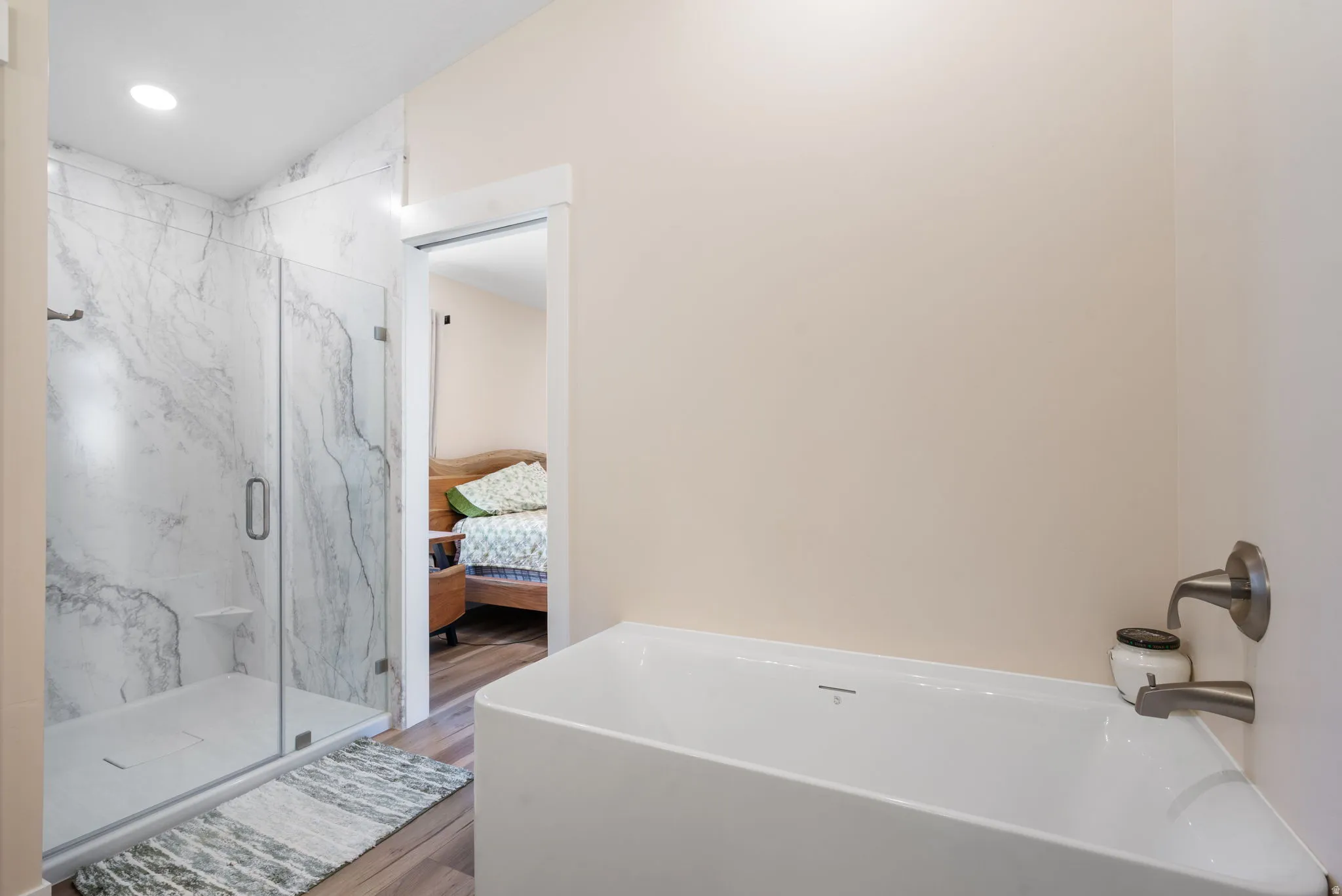 Freestanding soaking tub with brushed nickel fixtures complemented by a glass-enclosed shower featuring large format marble-look tile and a recessed light