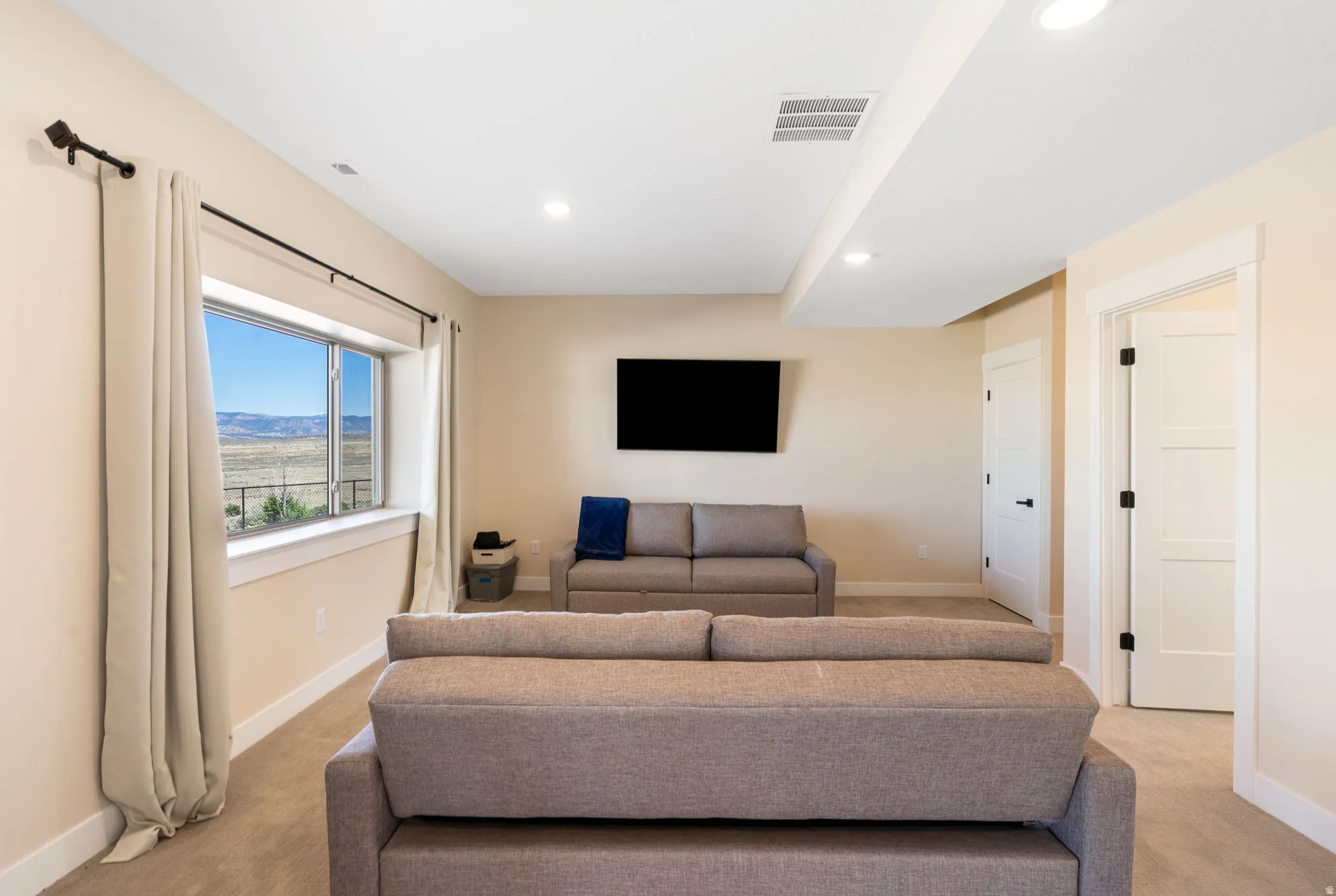 Recessed lighting illuminates this room, featuring light-toned walls and neutral carpeting